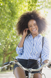 Begeisterte Frau mit Afro, die Fahrrad fährt und über Kopfhörer Musik hört - CAIF12335