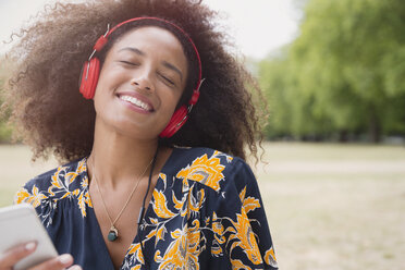 Begeisterte Frau, die mit Kopfhörern und mp3-Player im Park Musik hört - CAIF12342