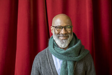 Porträt eines lächelnden Mannes mit Brille und Schal vor einem roten Vorhang - FMKF04910