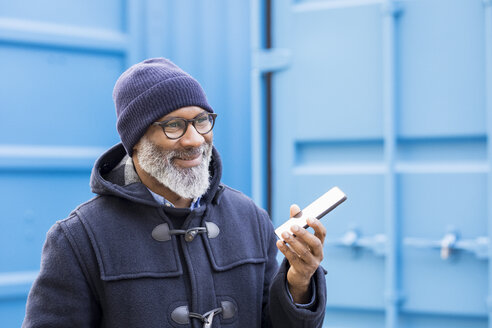 Porträt eines lächelnden Mannes, der ein Mobiltelefon im Freien benutzt - FMKF04915