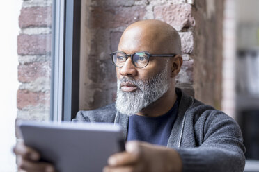 Portrait of pensive man with tablet looking out of window - FMKF04919