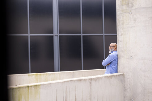 Pensive businessman leaning against concrete wall - FMKF04940