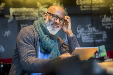 Portrait of smiling man with tablet in a coffee shop - FMKF04944