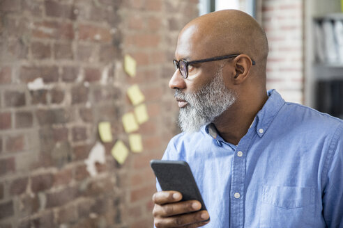 Businessman with cell phone in a loft - FMKF04947