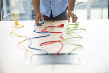 Close-up of businessman choosing from multicolored cables on table in conference room - FMKF04960