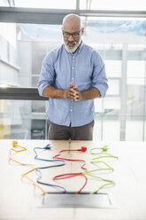 Businessman looking at multicolored cables on table in conference room - FMKF04961