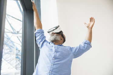 Businessman wearing VR glasses at the window - FMKF04962