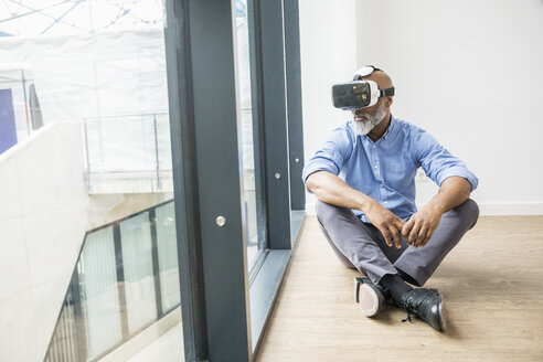 Geschäftsmann mit VR-Brille sitzt auf dem Boden am Fenster - FMKF04964