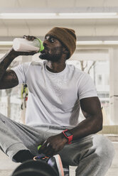 Mann sitzt auf einer Bank im Fitnessstudio und trinkt aus einer Flasche - UUF12980