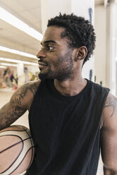 Man with tattoos holding basketball looking away - UUF12984