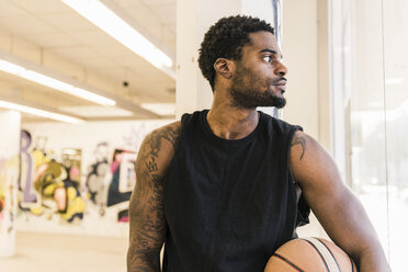 Mann mit Tattoos hält Basketball und schaut weg - UUF12985