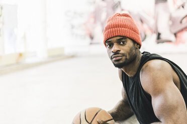 Man with tattoos and woolly hat holding basketball - UUF12988