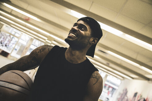 Lächelnder Mann mit Tattoos, der einen Basketball hält und zur Seite schaut - UUF12992