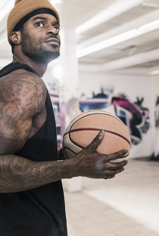 Mann mit Tattoos und Wollmütze hält Basketball, lizenzfreies Stockfoto