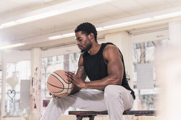 Man with tattoos sitting down holding basketball - UUF12994