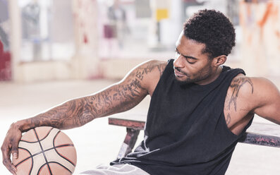 Man with tattoos sitting down holding basketball - UUF12998