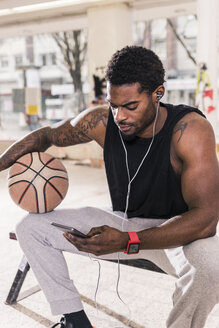 Mann mit Tattoos und Basketball mit Smartphone und Kopfhörern - UUF13000