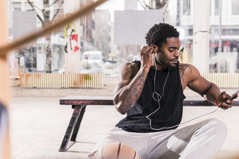 Mann mit Tattoos und Basketball mit Smartphone und Kopfhörern - UUF13001