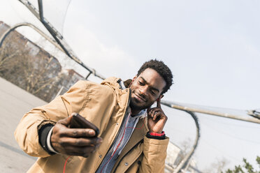 Smiling young man with smartphone and earphones outdoors - UUF13034