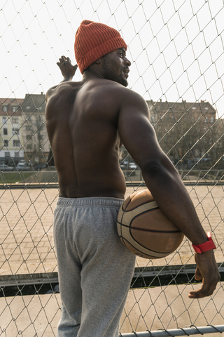 Rückansicht eines muskulösen, barbusigen Basketballspielers, der am Zaun steht, lizenzfreies Stockfoto