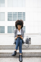 Smiling woman sitting on stairs outdoors using cell phone - JRFF01608