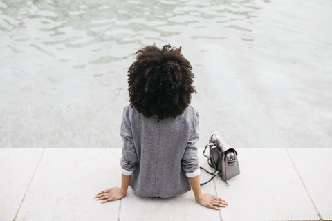 Rückenansicht einer Frau, die am Rande eines Pools sitzt, lizenzfreies Stockfoto