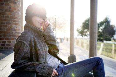 Portrait of woman wearing knit hat sitting on steps park - CAVF05603