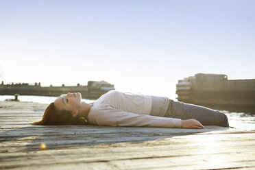 Side view of woman lying on pier against clear sky - CAVF05605