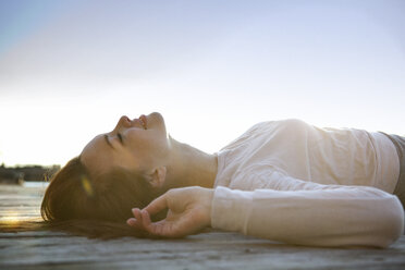 Side view of woman relaxing on pier against sky - CAVF05606