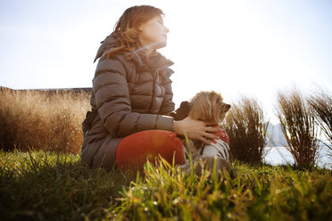 Niedriger Blickwinkel auf eine Frau mit Hund, die auf einem Feld vor einem klaren Himmel sitzt - CAVF05613