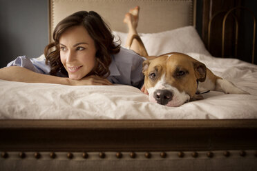 Woman looking away while relaxing with dog on bed at home - CAVF05620