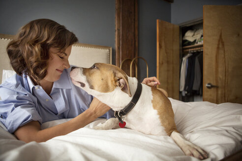 Lächelnde Frau spielt mit Hund auf Bett zu Hause - CAVF05623