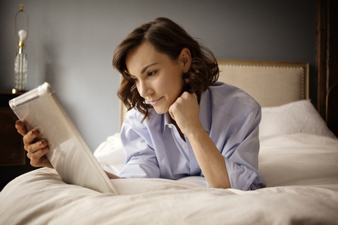 Frau benutzt Tablet-Computer, während sie zu Hause auf dem Bett liegt, lizenzfreies Stockfoto