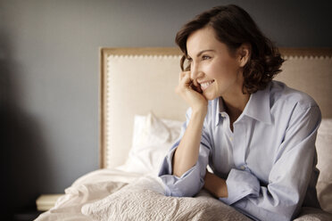 Woman with hand on chin looking away while sitting on bed at home - CAVF05625