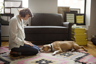 Woman looking at dog lying on carpet - CAVF05626