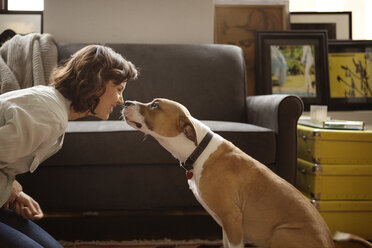 Woman rubbing nose with dog at home - CAVF05628