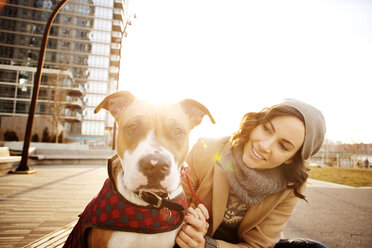 Woman looking at dog while sitting on bench against clear sky - CAVF05633