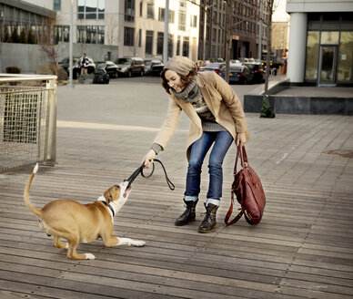 Hund auf Frau, die auf einem Fußweg in der Stadt an der Leine zieht - CAVF05635