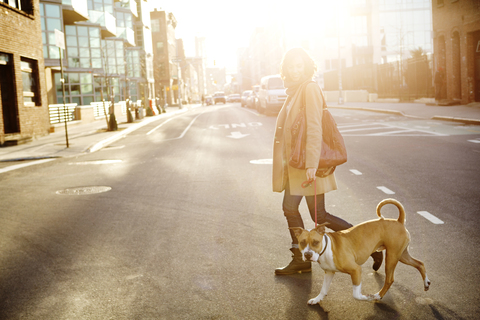 Seitenansicht einer Frau mit Hund beim Überqueren der Straße in der Stadt, lizenzfreies Stockfoto
