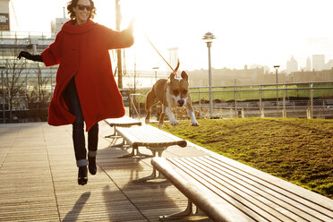 Frau läuft mit Hund und springt auf Bänke im Park - CAVF05638