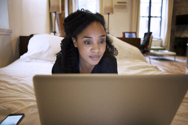 Frau, die einen Laptop benutzt, während sie auf dem Bett liegt - CAVF05642