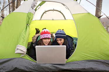 Friends using laptop computer while lying in tent - CAVF05658