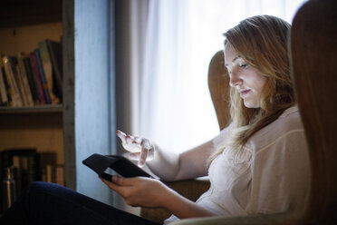 Frau benutzt Tablet-Computer, während sie zu Hause auf einem Sessel sitzt - CAVF05675