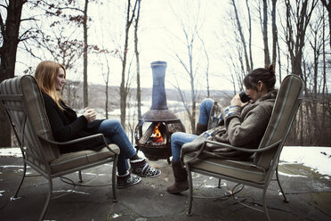 Freunde, die am Lagerfeuer sitzen und sich unterhalten und ein Getränk genießen - CAVF05714