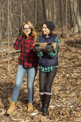 Woman carrying firewood while walking with friend in forest - CAVF05731