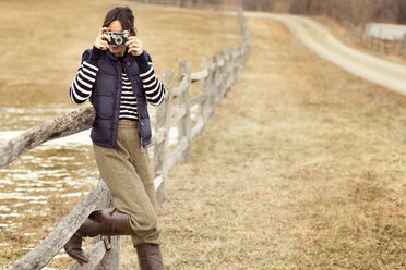 Frau beim Fotografieren an einem Holzgeländer auf einem Feld stehend - CAVF05735