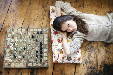 Porträt einer Frau auf dem Boden liegend neben einem Schachbrett zu Hause - CAVF05750