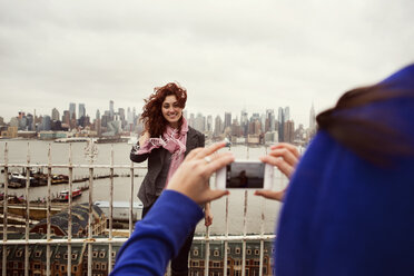 Cropped image of friend photographing woman standing by railing against city - CAVF05829