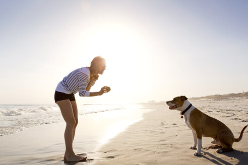 Seitenansicht einer Frau, die mit ihrem Hund spielt, während sie am Strand steht - CAVF05858
