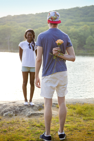 Rückansicht eines Mannes, der eine Rose hinter seinem Rücken versteckt, um seiner Freundin einen Antrag zu machen, lizenzfreies Stockfoto